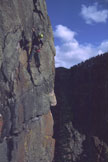 A climber on a vertical cliff beneath blue sky